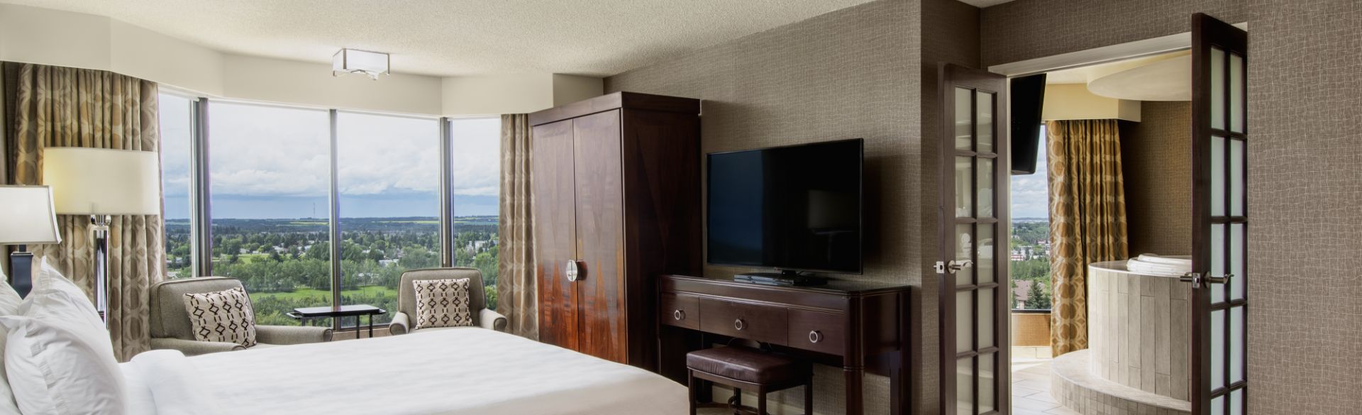 This inviting and expansive suite offers a picturesque natural view through its generous windows, adorned with exquisite wooden furniture. The adjoining bathroom features a luxurious jacuzzi bathtub, conveniently located near the bedroom.